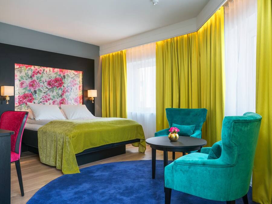 Una camera d'albergo con un letto, una scrivania, due sedie, un tavolino rotondo e un grande dipinto floreale sulla parete.
