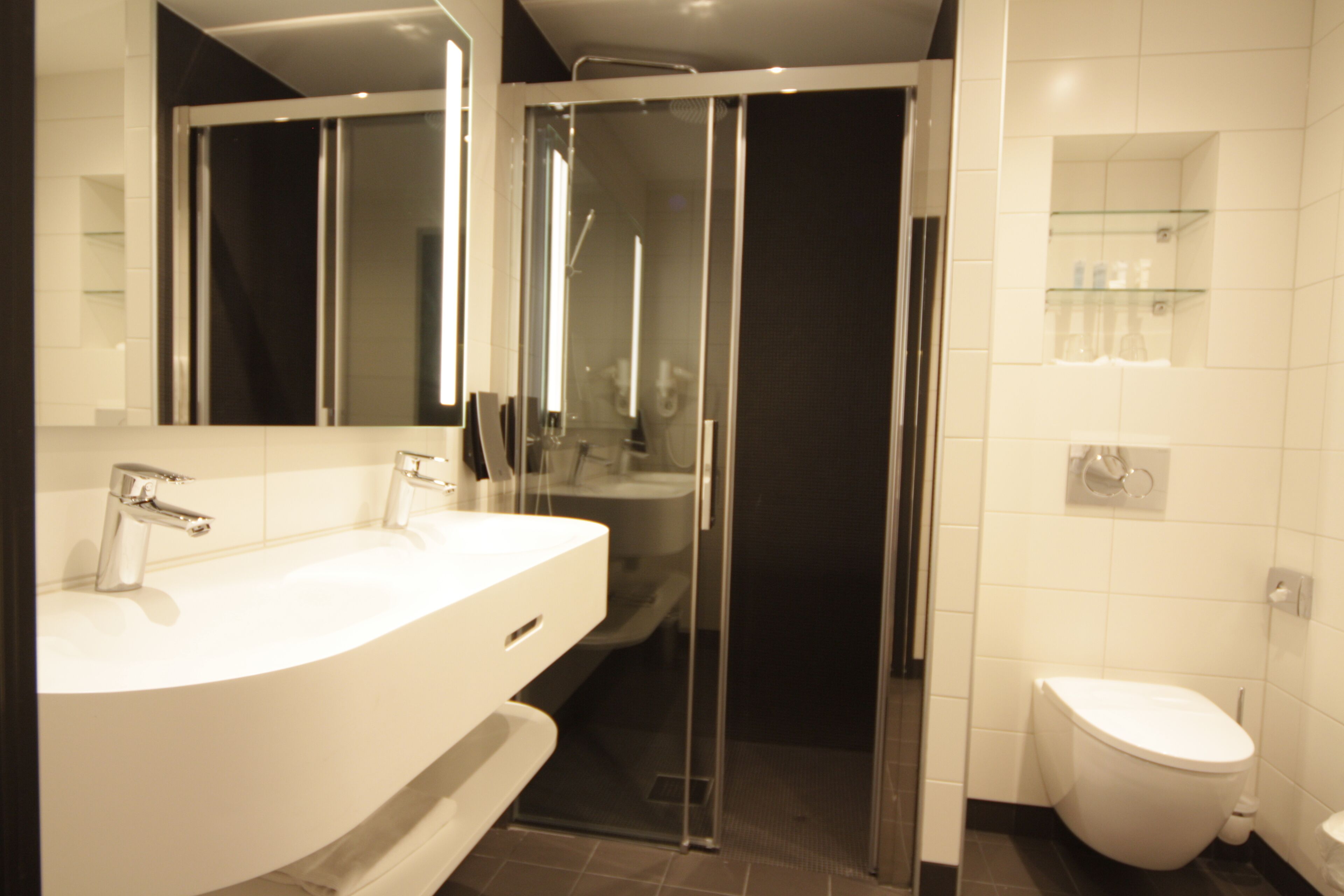 A modern bathroom with a large white sink, a glass shower enclosure, and a white toilet.