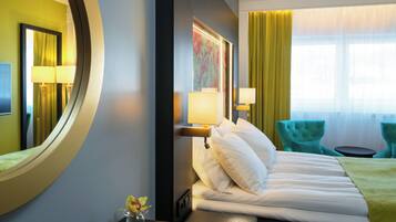 A hotel room with a bed, two chairs, a round mirror, and a window with curtains.