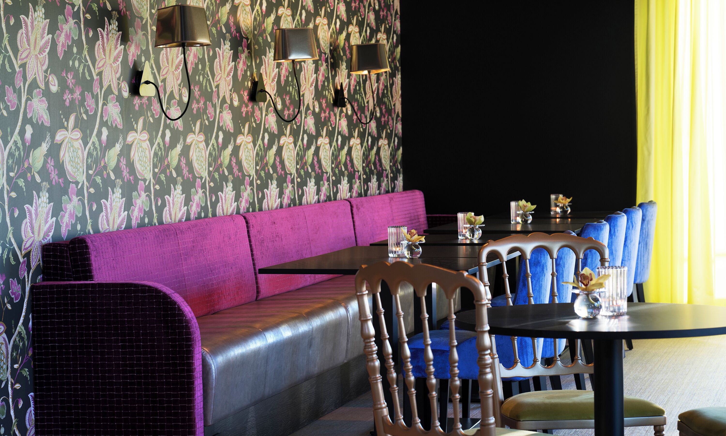 A restaurant interior with a purple sofa, blue chairs, and a table with candles.