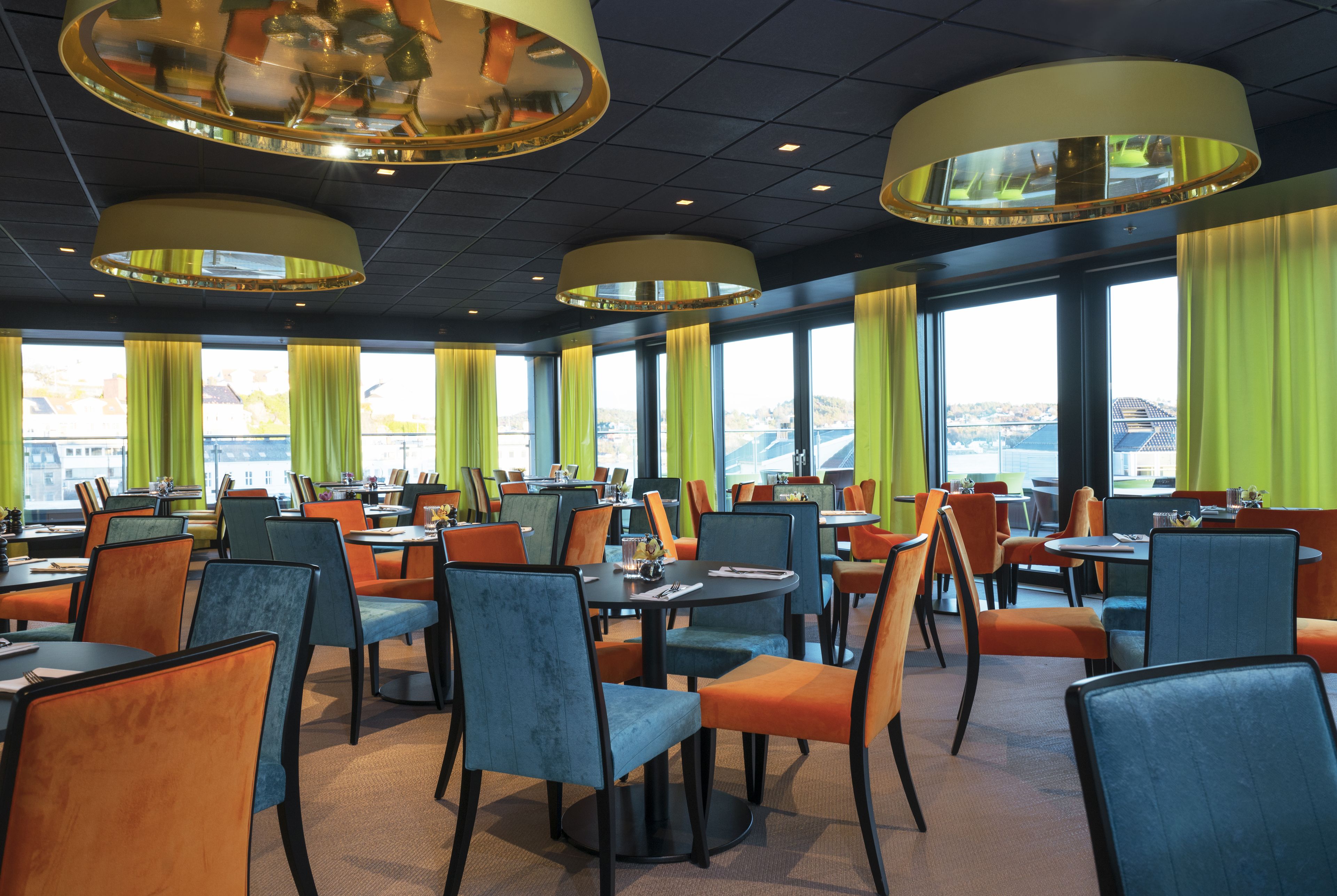 Un restaurante con varias mesas y sillas, amplias ventanas con cortinas y vistas a un puente.