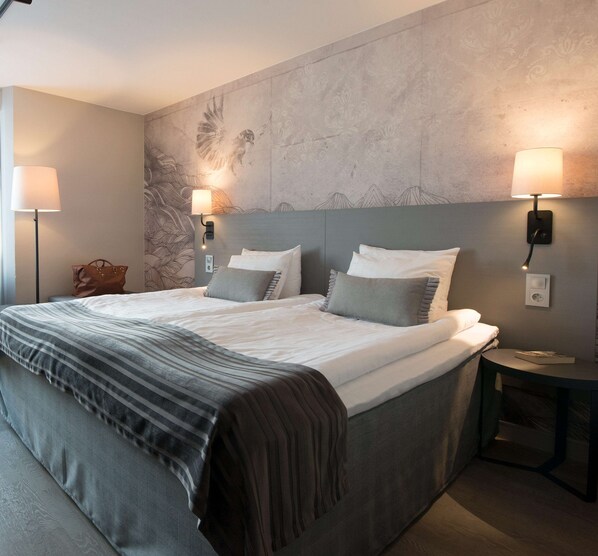 A modern hotel room with a large bed, two bedside lamps, a nightstand, and a decorative wall.