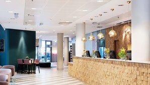 A modern reception area with a wooden reception desk, seating area, and a patterned floor. - Scandic Crown (Gothenburg)