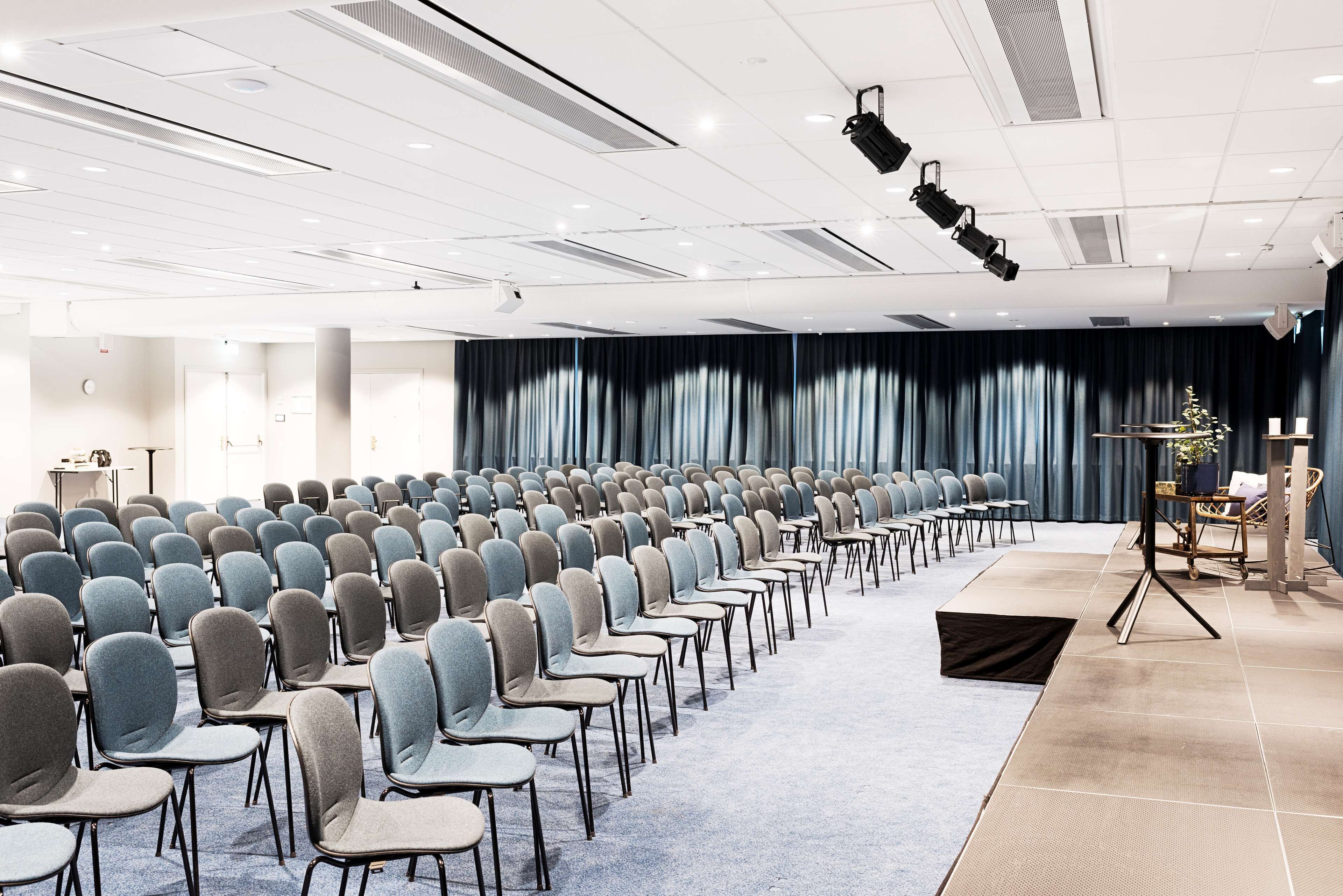 Ett konferensrum med rader av stolar, en scen med draperier och ett talarstånd.