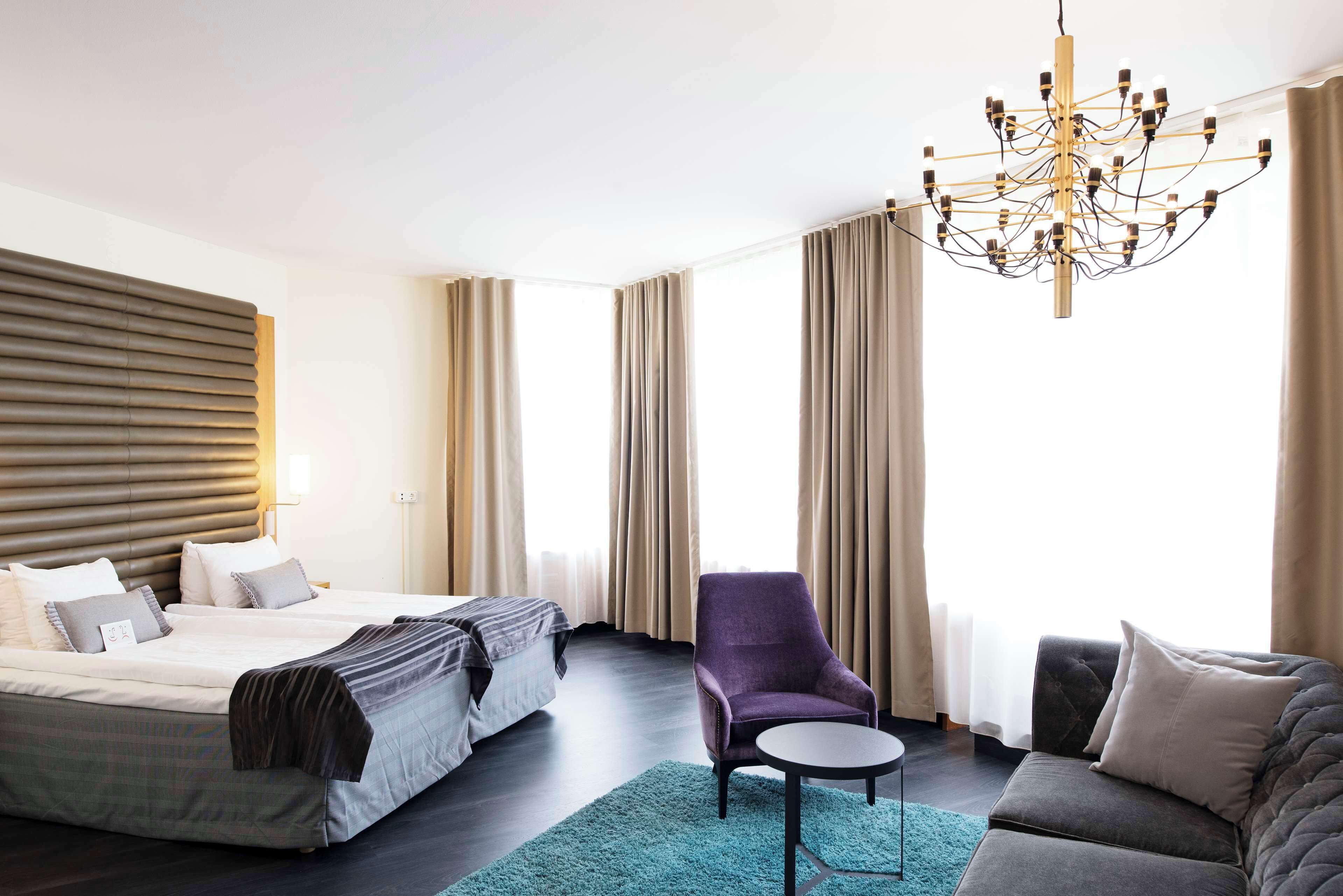 Ett hotellrum med en stor säng, en stol, en soffa och en kristallkrona.