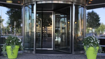 Una puerta giratoria con paneles de vidrio y dos plantas en macetas a cada lado.