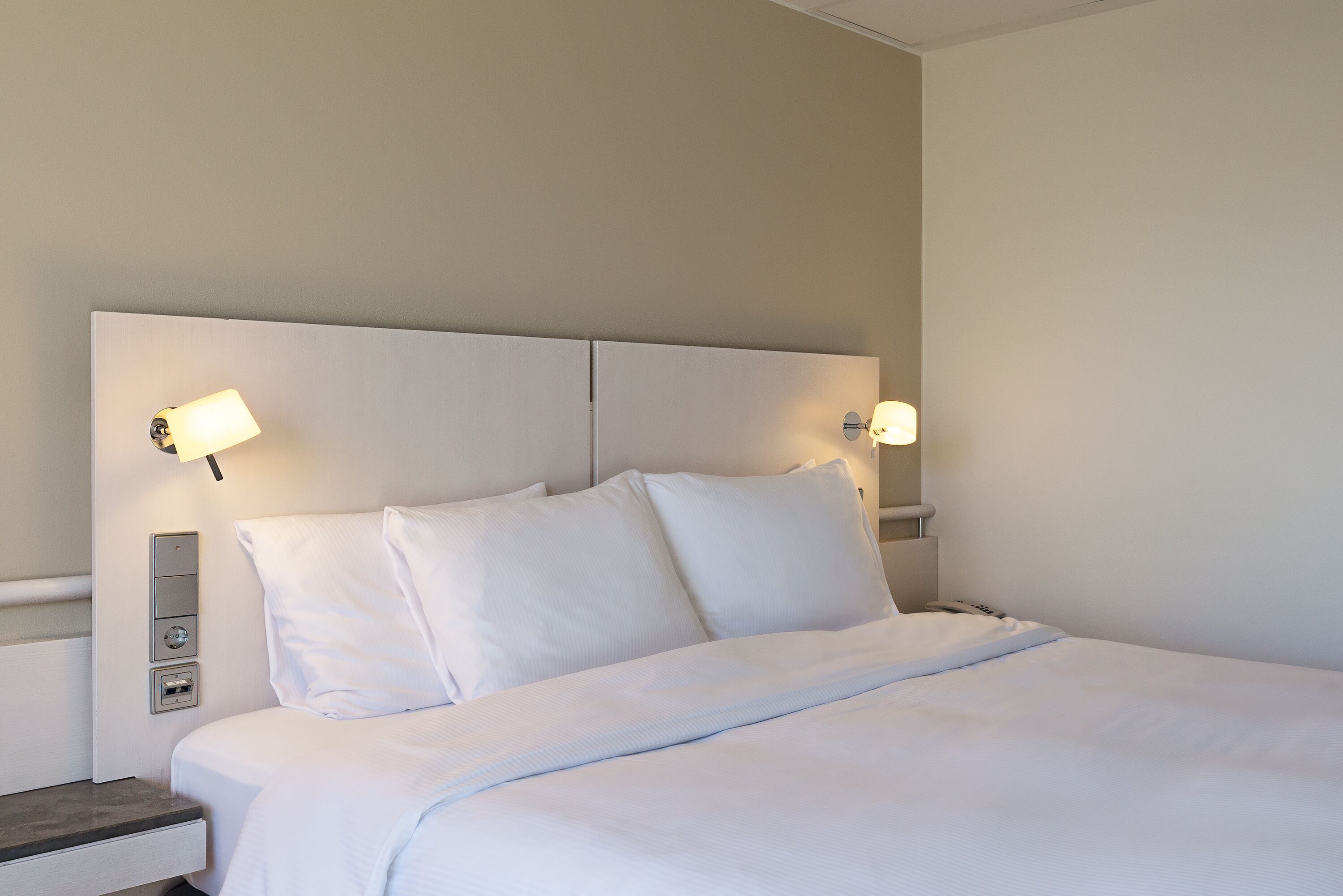 A neatly made bed with white linens, a headboard, and bedside lamps.