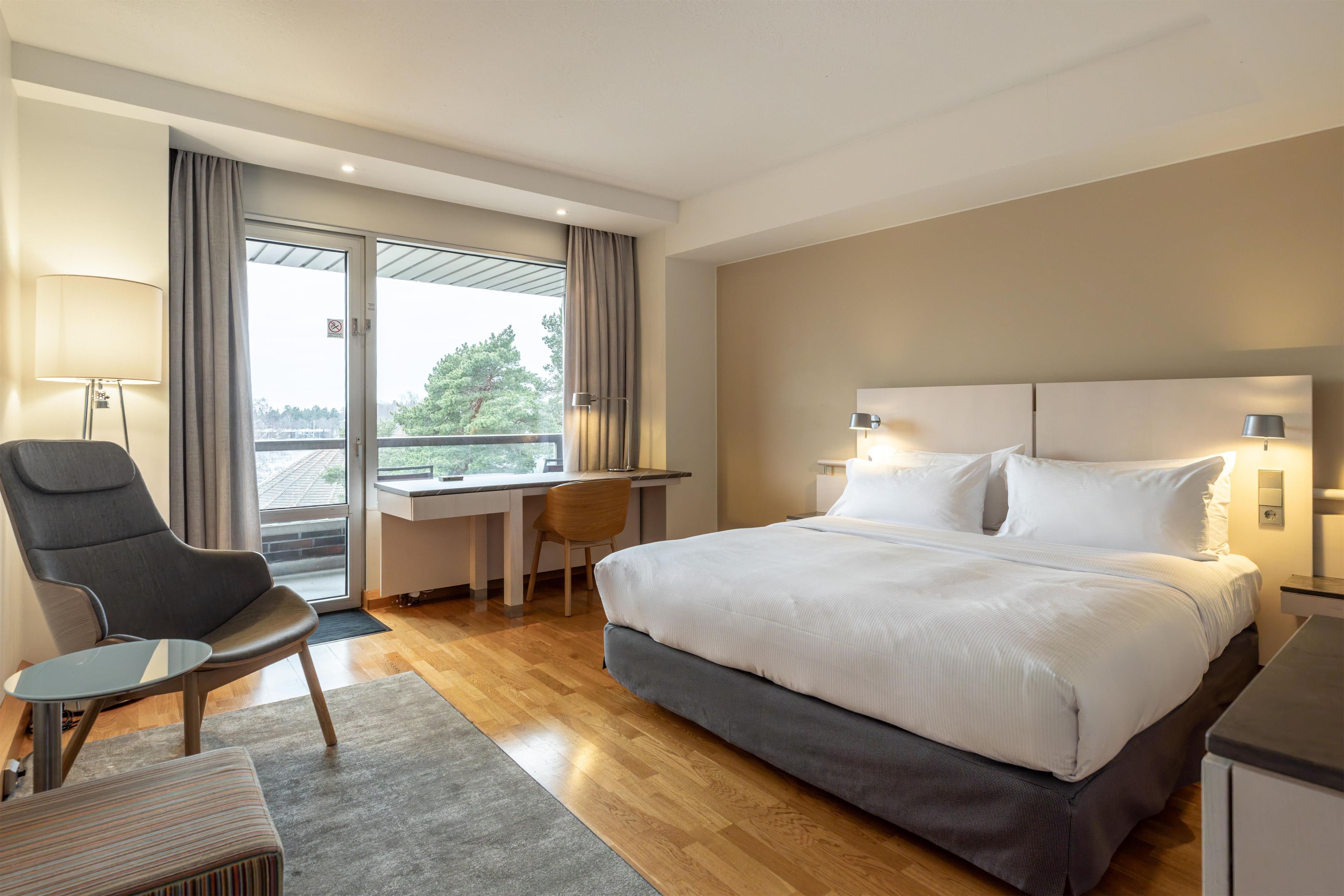Habitación de hotel con cama, escritorio, silla y vistas a través de una ventana.