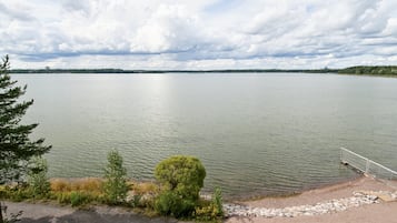 A calm lake with a sandy shore and a metal railing.