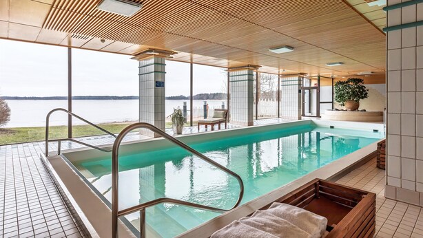 A swimming pool with a view of a lake, surrounded by tiled walls and wooden beams on the ceiling. - Hilton Helsinki Kalastajatorppa (Helsinki)
