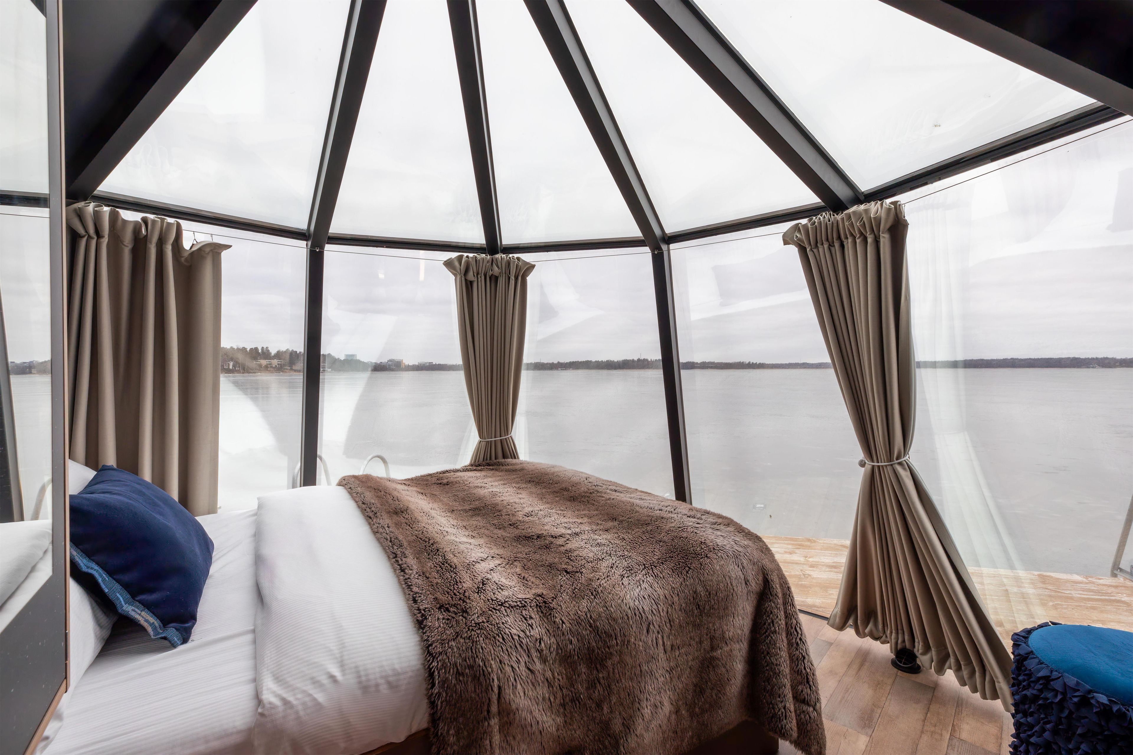 A room with a bed, a view of a body of water, and a glass ceiling structure.