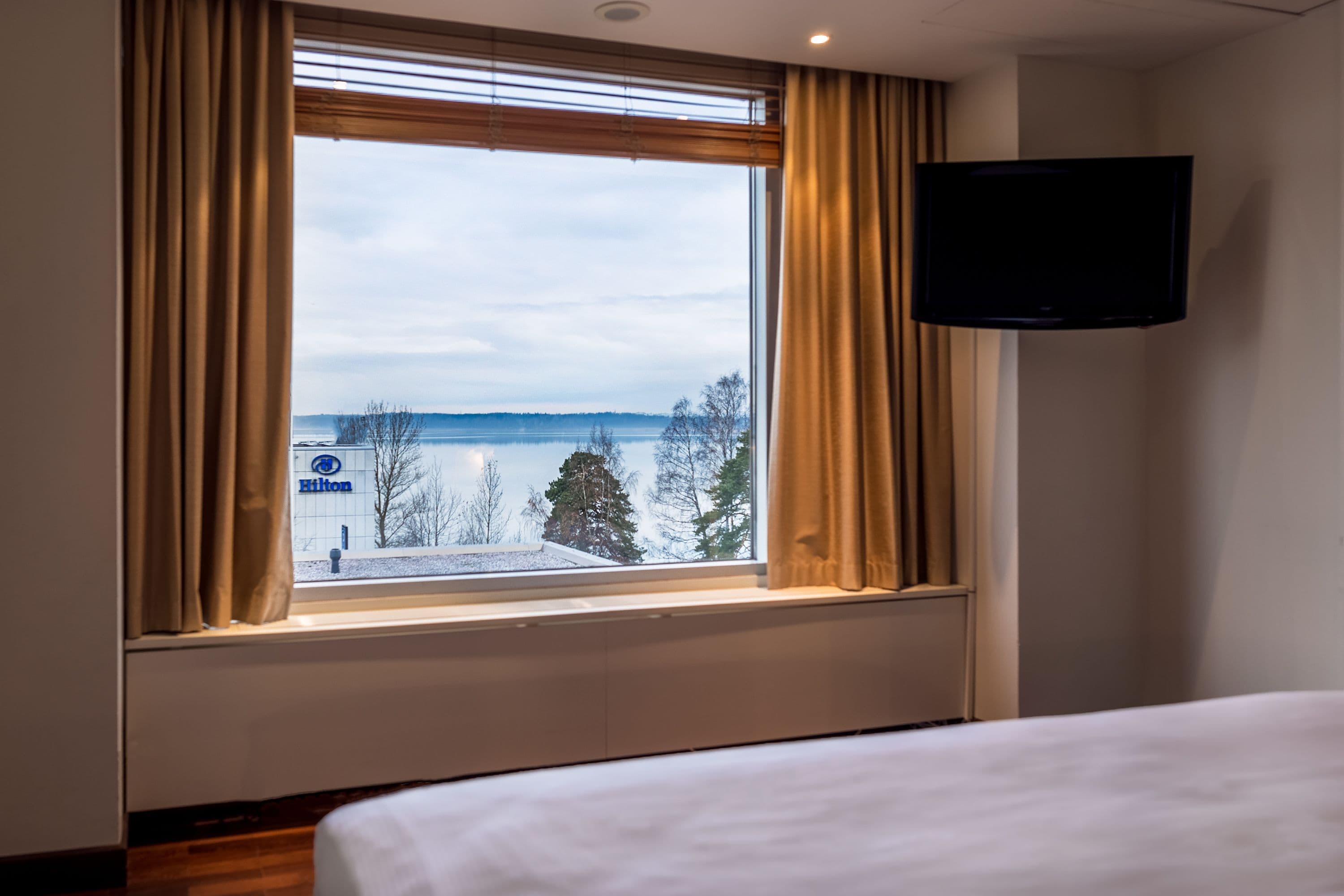 Ett hotellrum med ett stort fönster, en säng och en platt-TV som är monterad på väggen.