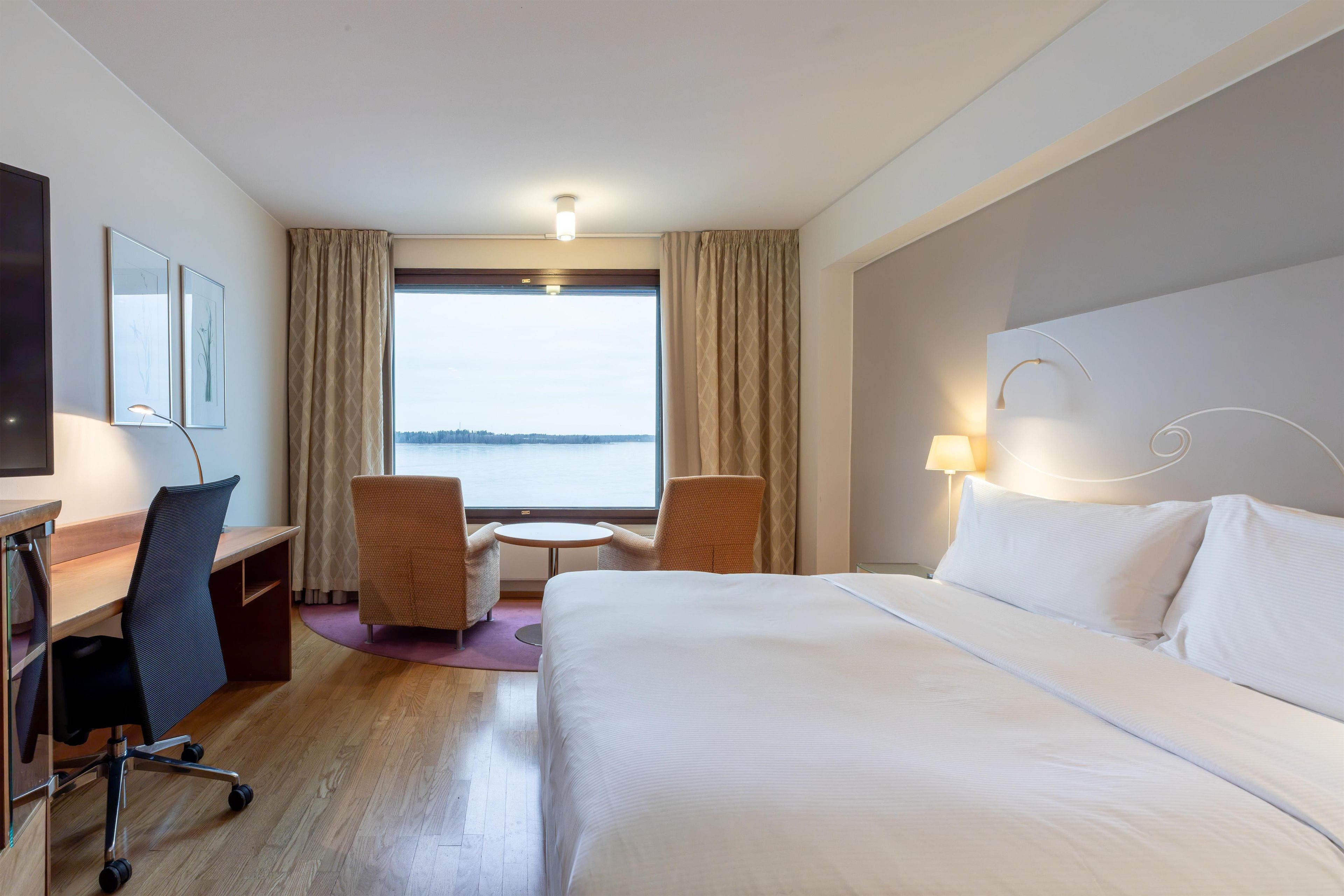 Habitación de hotel con cama, escritorio, sillas y un ventanal que ofrece vistas.