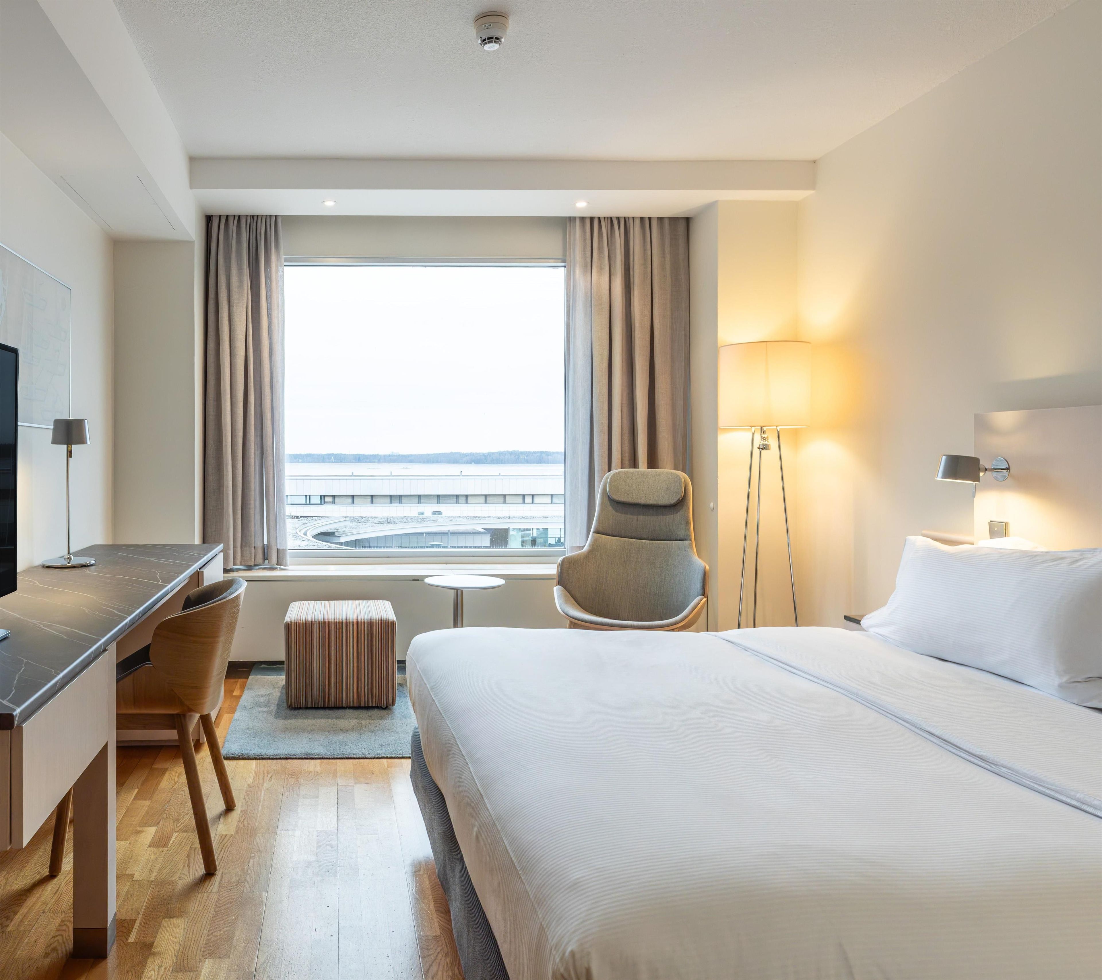 Hotellihuone, jossa on sänky, työpöytä, tuoli ja näkymä ulos.