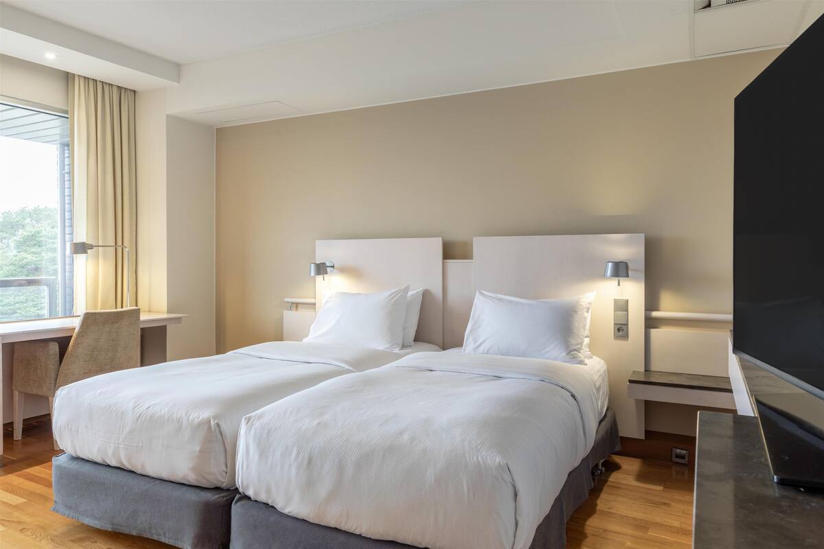 Ein modernes Hotelzimmer mit zwei Betten, einem Schreibtisch und einem Fernseher.