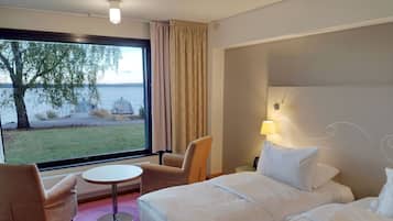 Ein Hotelzimmer mit großem Fenster, einem Bett, einem Sessel, einem kleinen Tisch und einer Lampe.