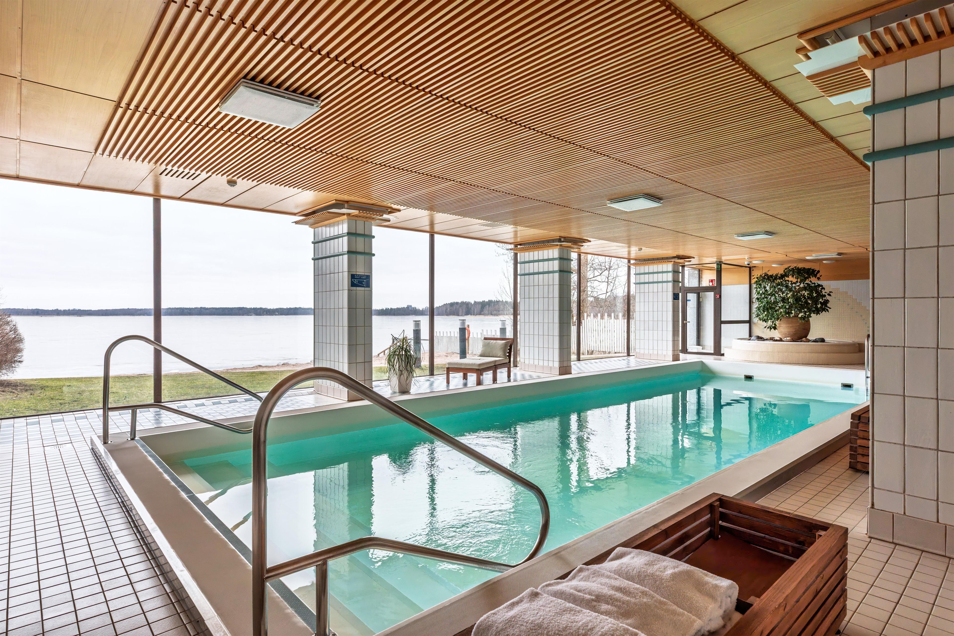 An indoor swimming pool with clear views of a lake and a wooden ceiling design.