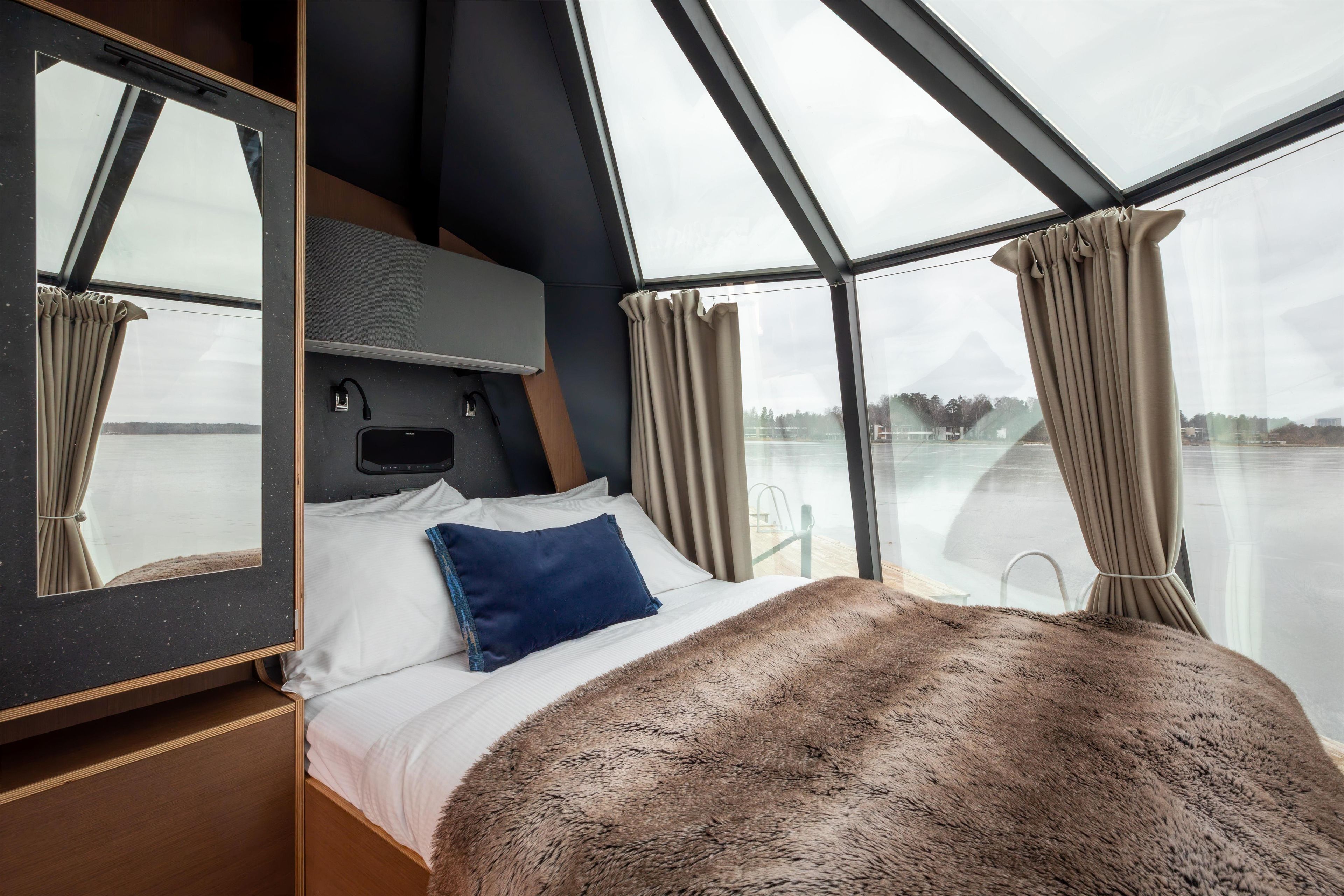 A modern interior with a bed, a headboard, a mirror, and a view of a body of water through large windows.