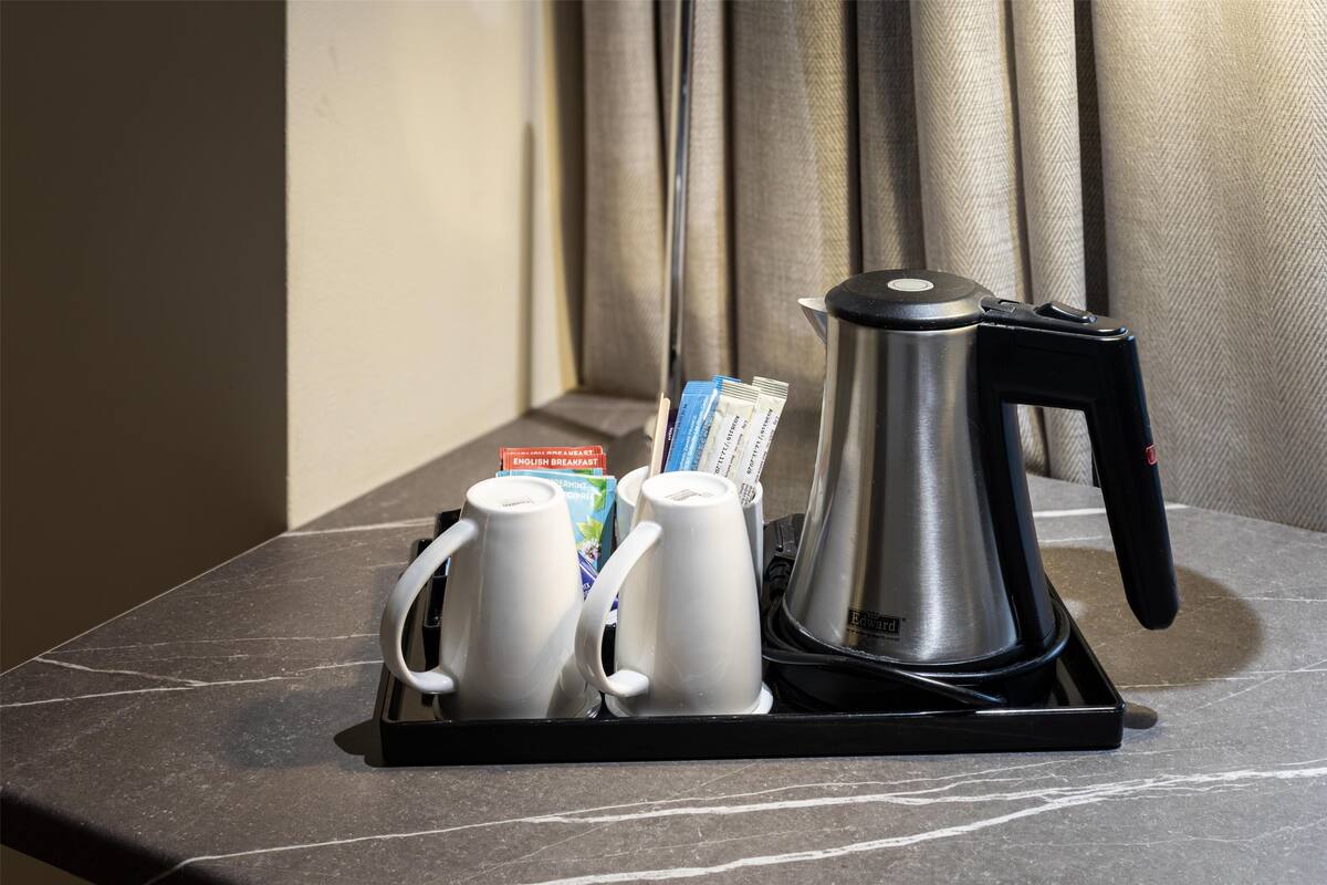 Ein Tablett mit einer Kaffeemaschine, zwei weißen Tassen und verschiedenen Frühstücksangeboten auf einer Marmorarbeitsplatte.