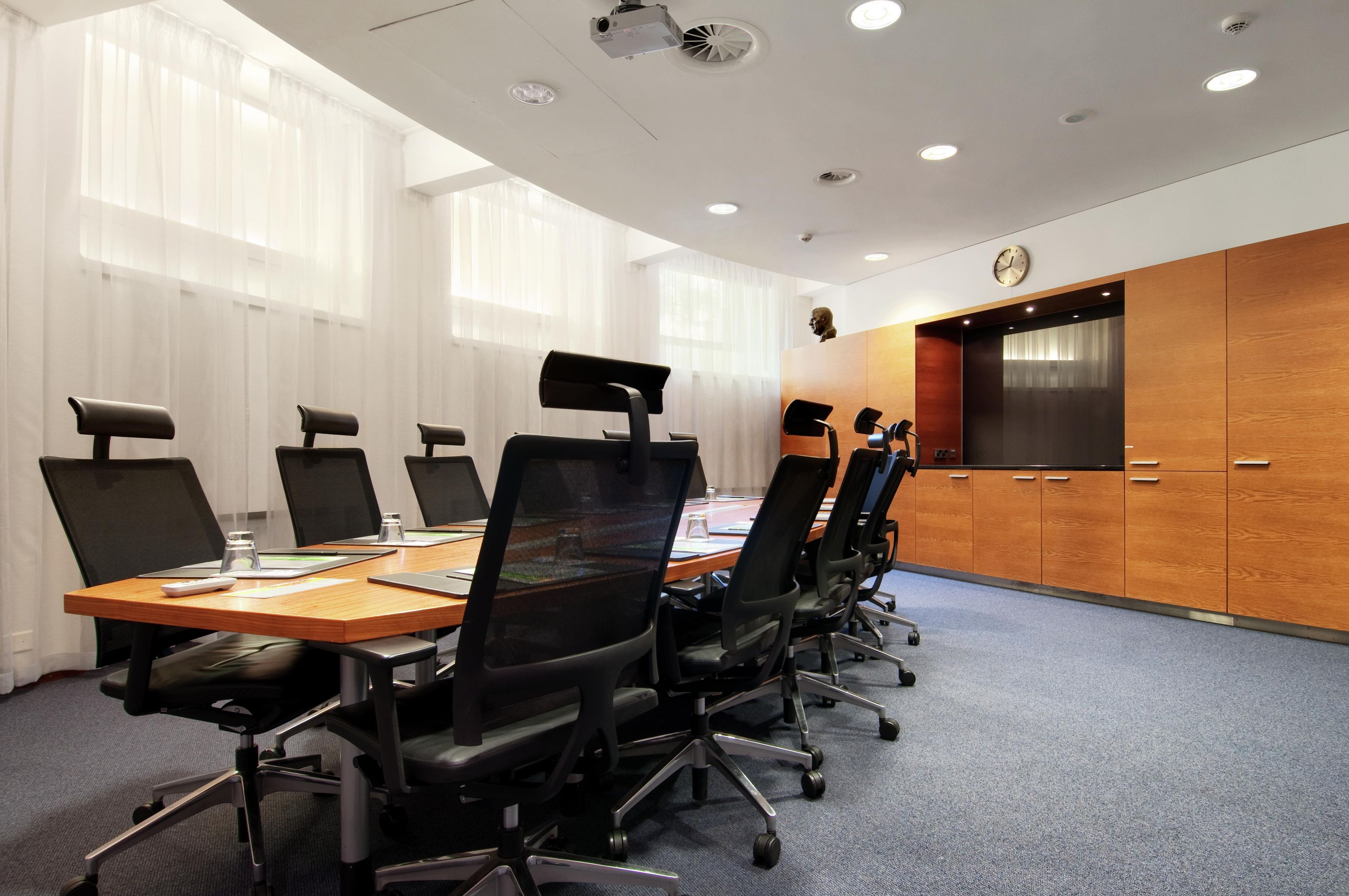 A conference room with a long table, black chairs, a wooden cabinet, and a clock on the wall.