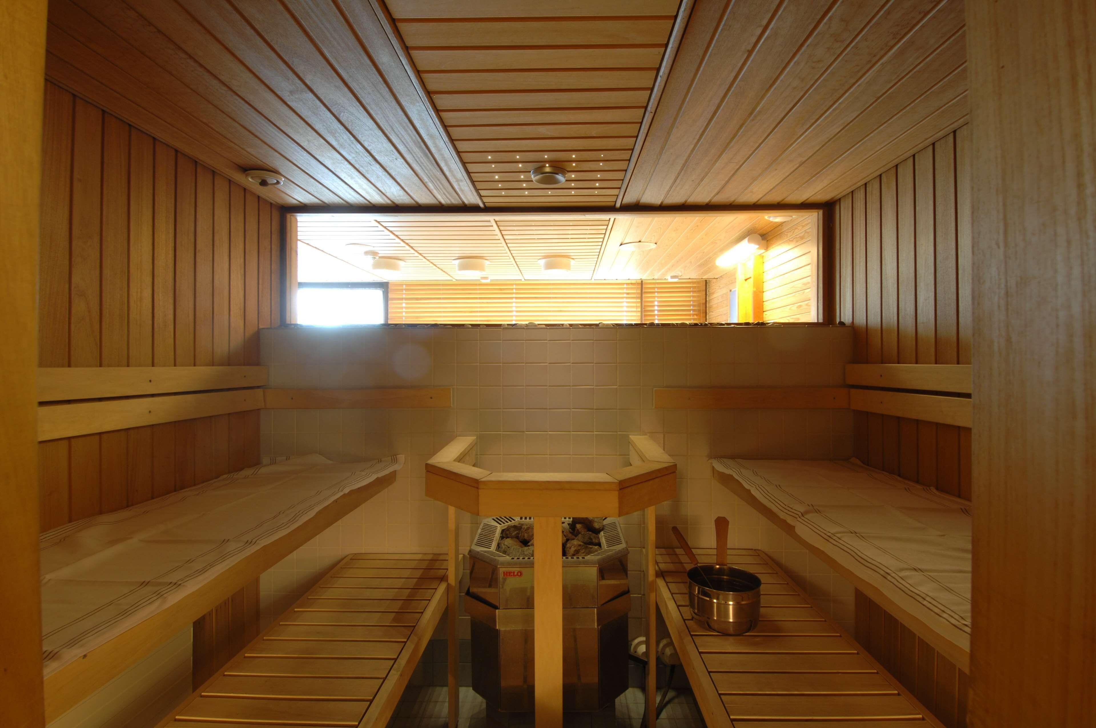 En sauna med træbænke, et centralt bord med ovn, og et vindue der lukker naturligt lys ind.