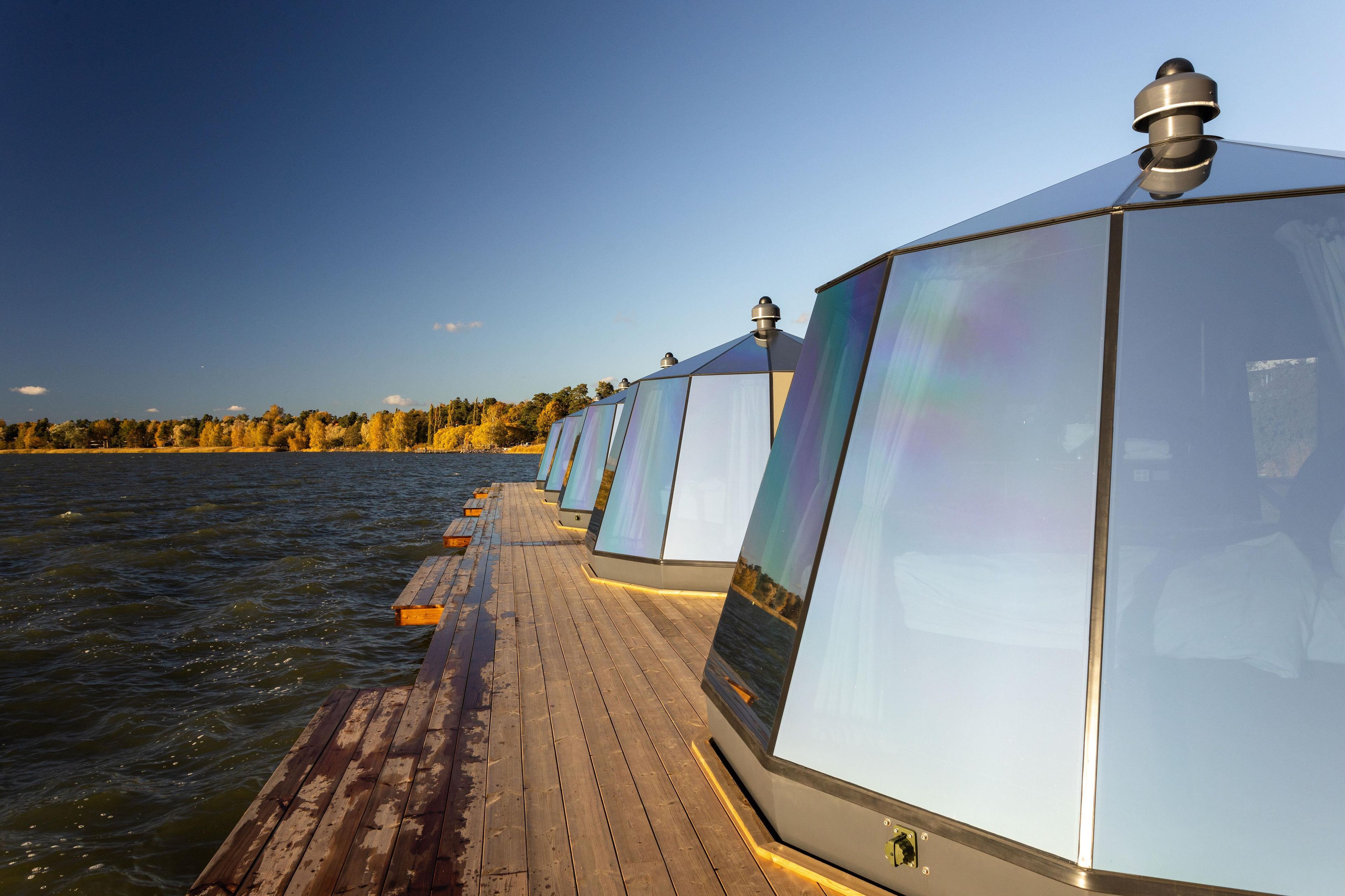 Een rij glazen constructies met een houten terras dat in het water uitloopt.