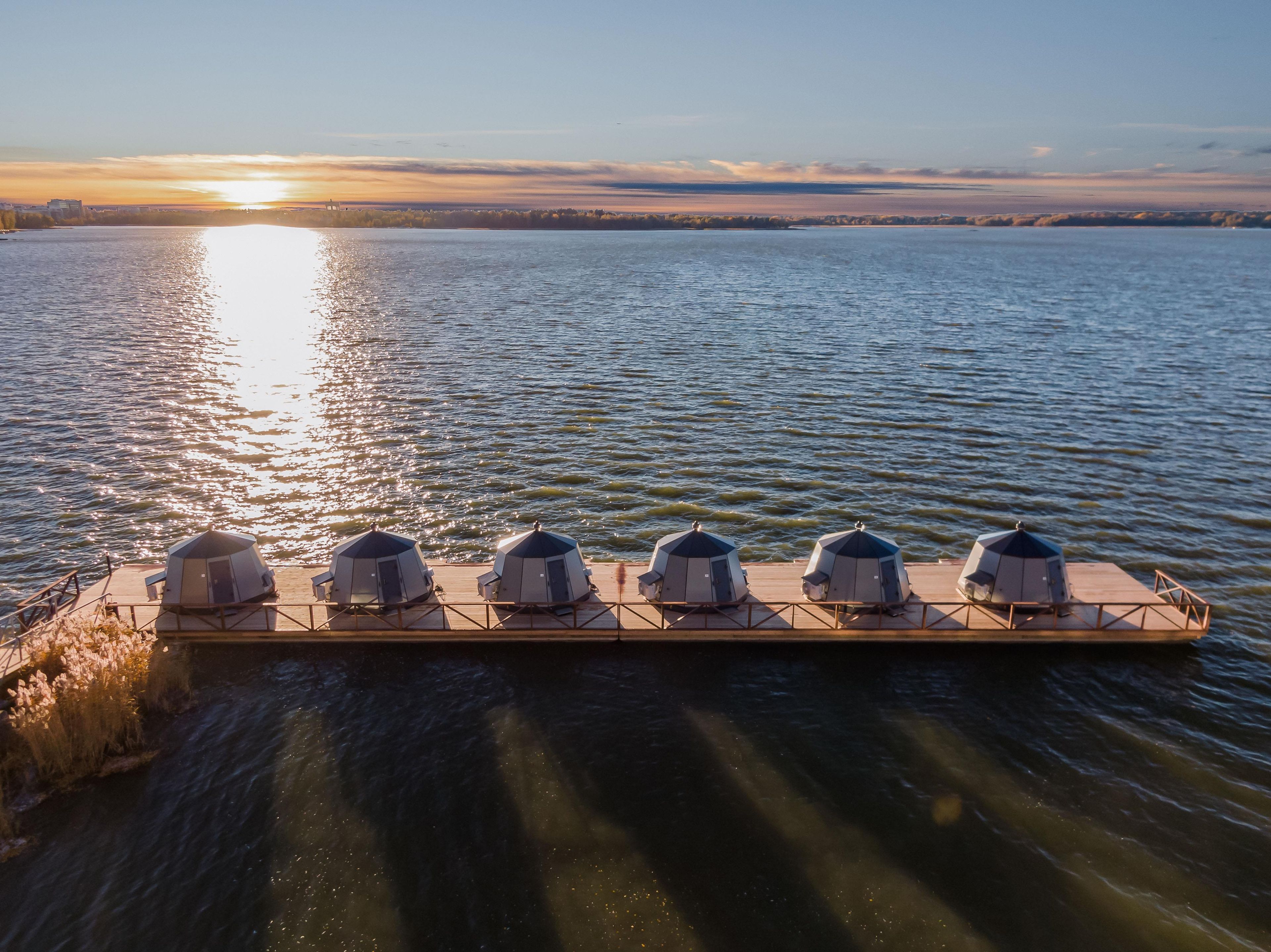 A floating platform with five dome-shaped structures, likely for accommodation, over a body of water with a sunset in the background.