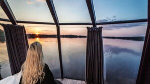 A person seated by a large window overlooking a calm lake at sunset. - Hilton Helsinki Kalastajatorppa (Helsinki)