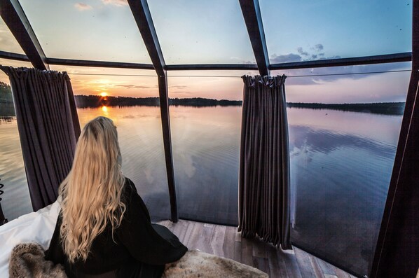 A person seated by a large window overlooking a calm lake at sunset. - Hilton Helsinki Kalastajatorppa (Helsinki)