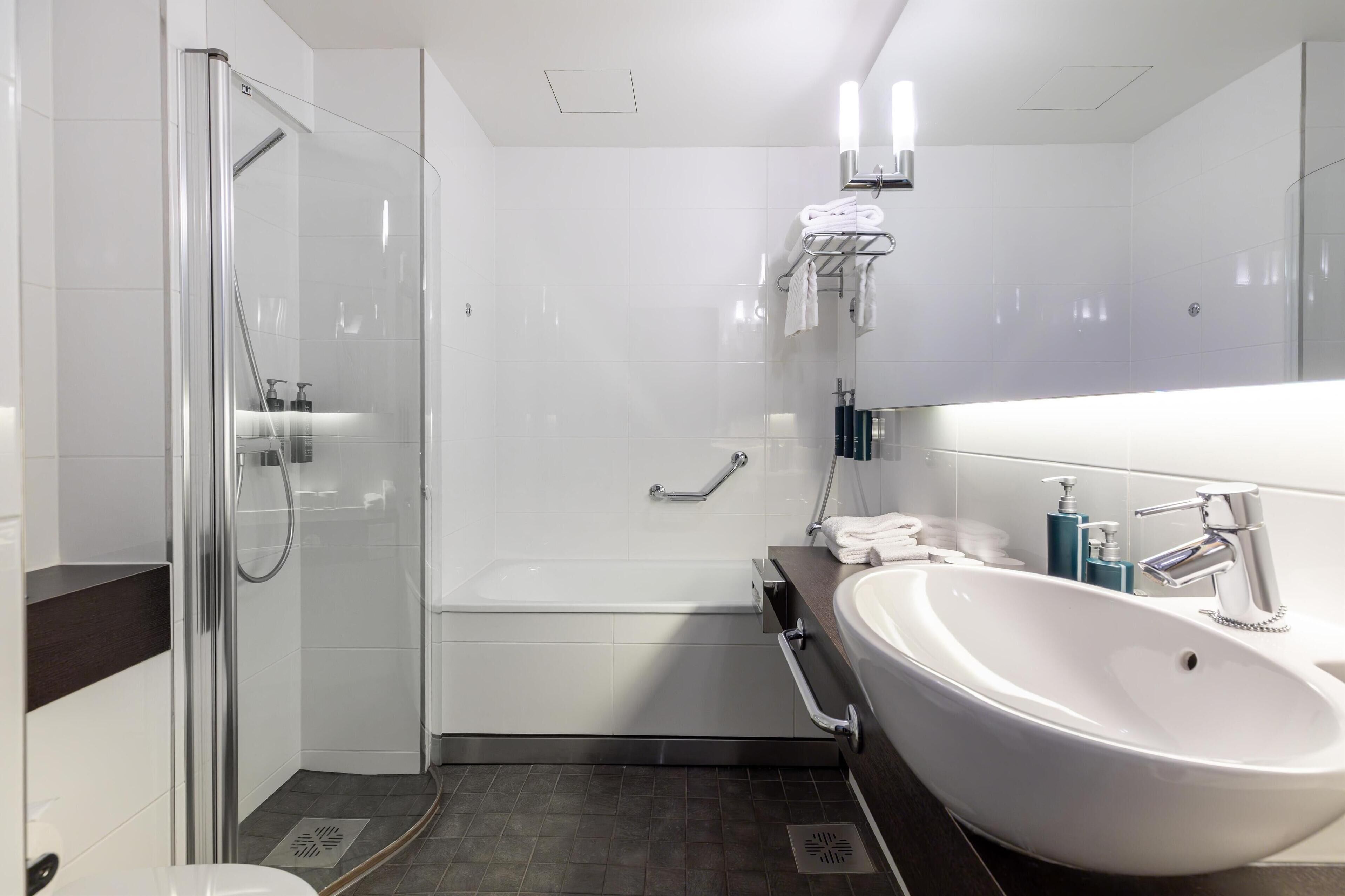A modern bathroom with a glass-enclosed shower, a bathtub, a large sink, and a vanity with a mirror.