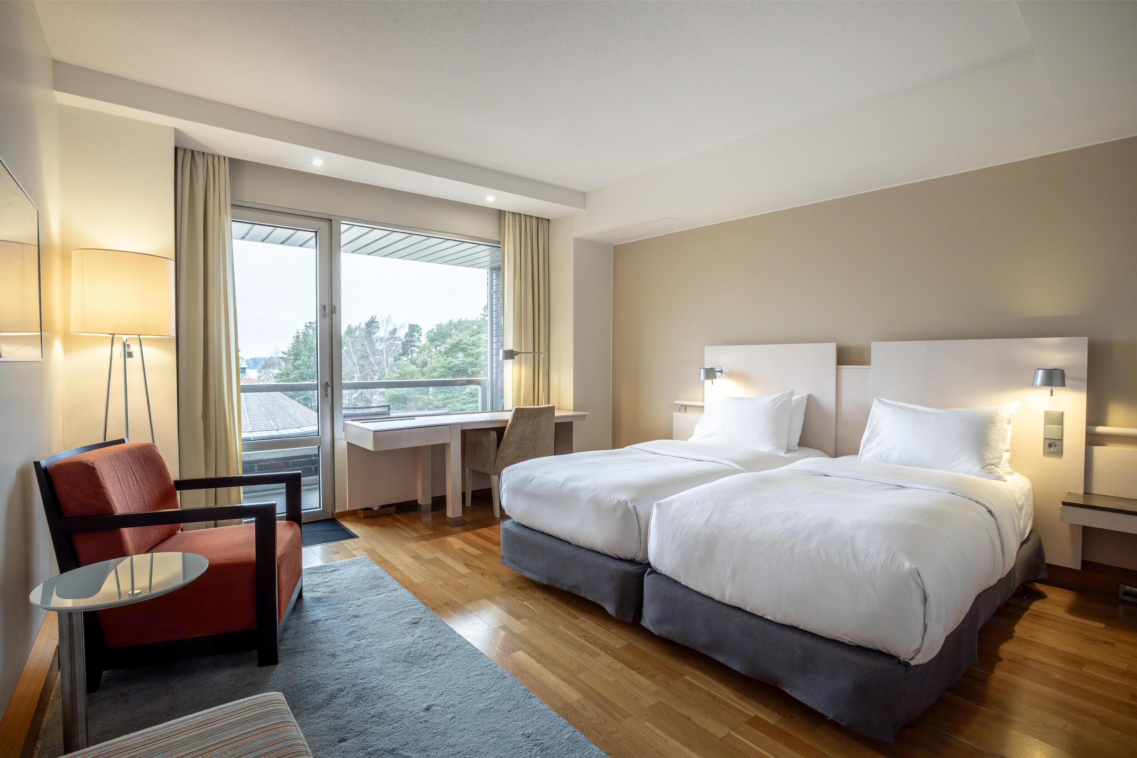 Une chambre d’hôtel avec deux lits, un bureau, une chaise et une grande fenêtre.