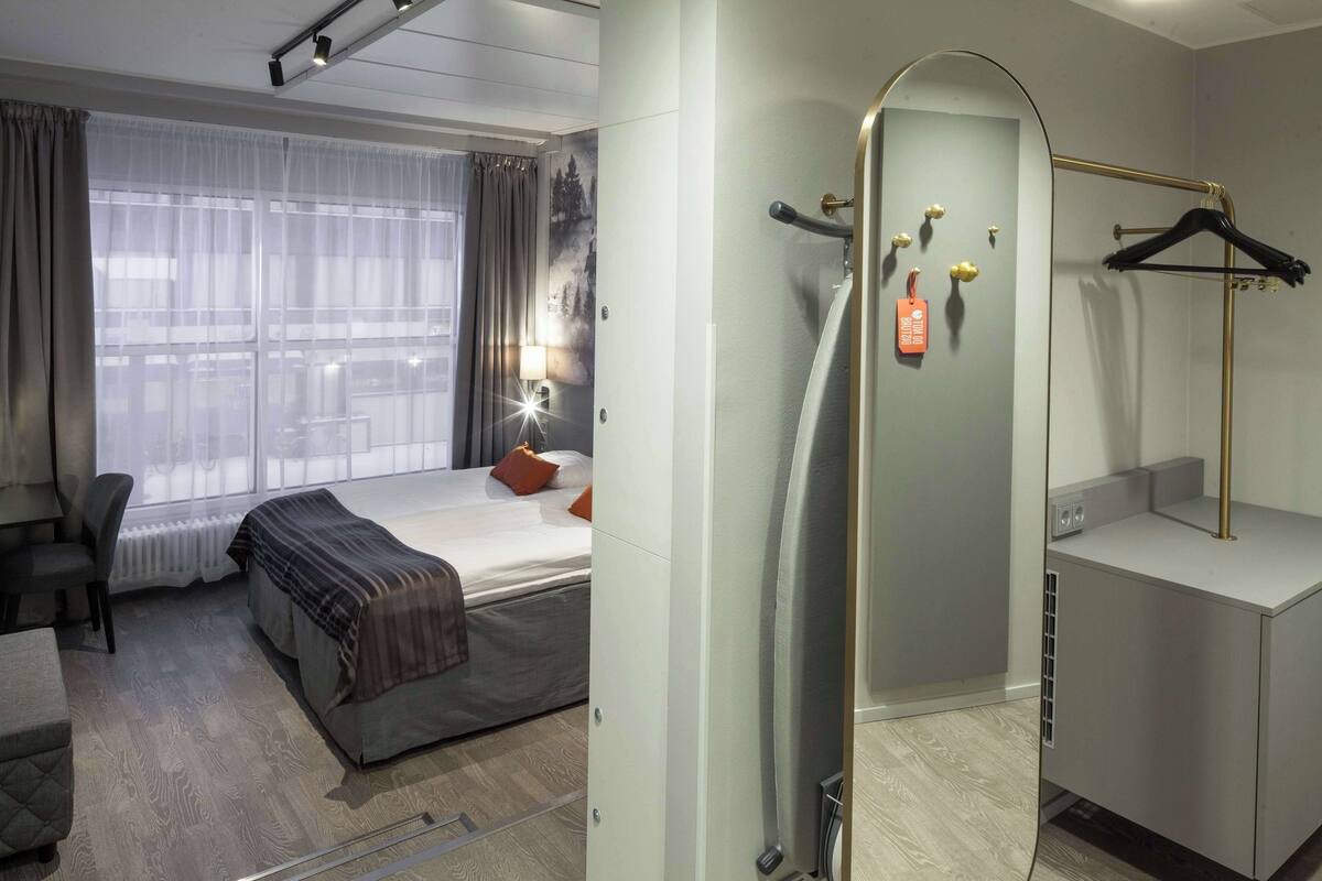 A hotel room with a bed, a desk, a chair, a wardrobe, and a shower area.