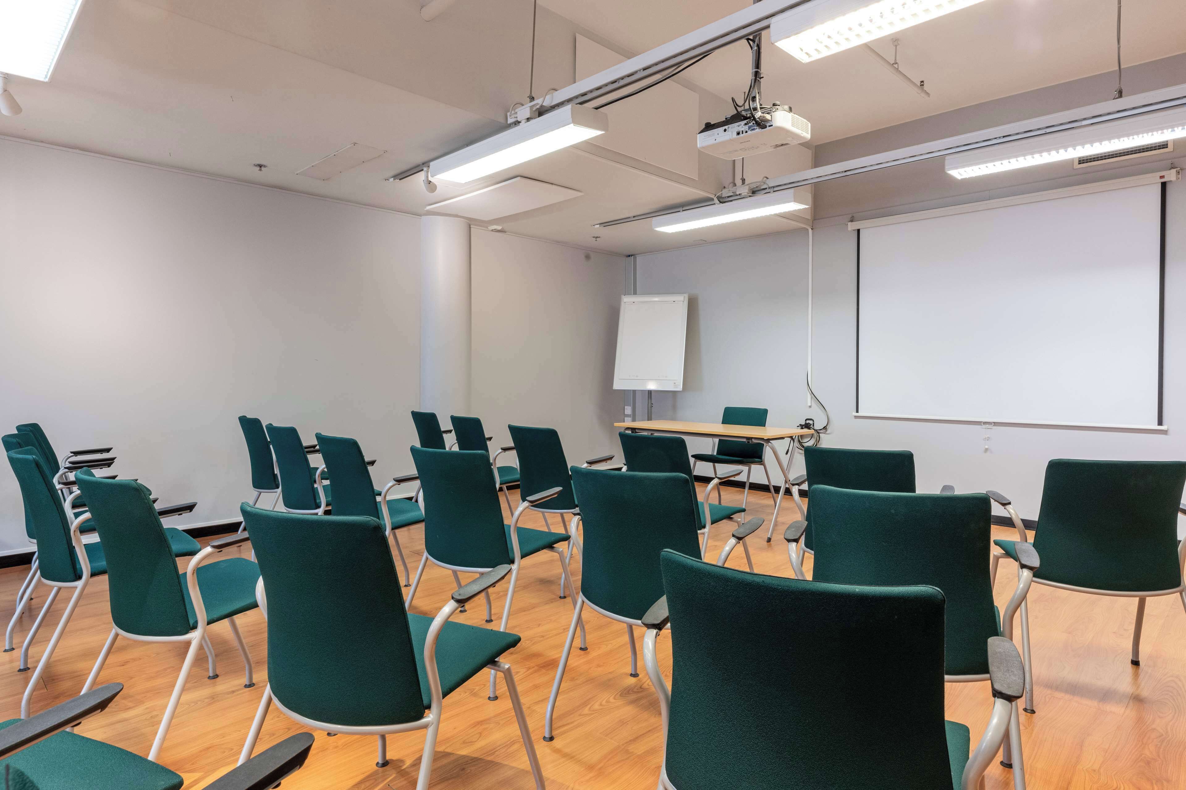A classroom with green chairs, a whiteboard, and a projector.