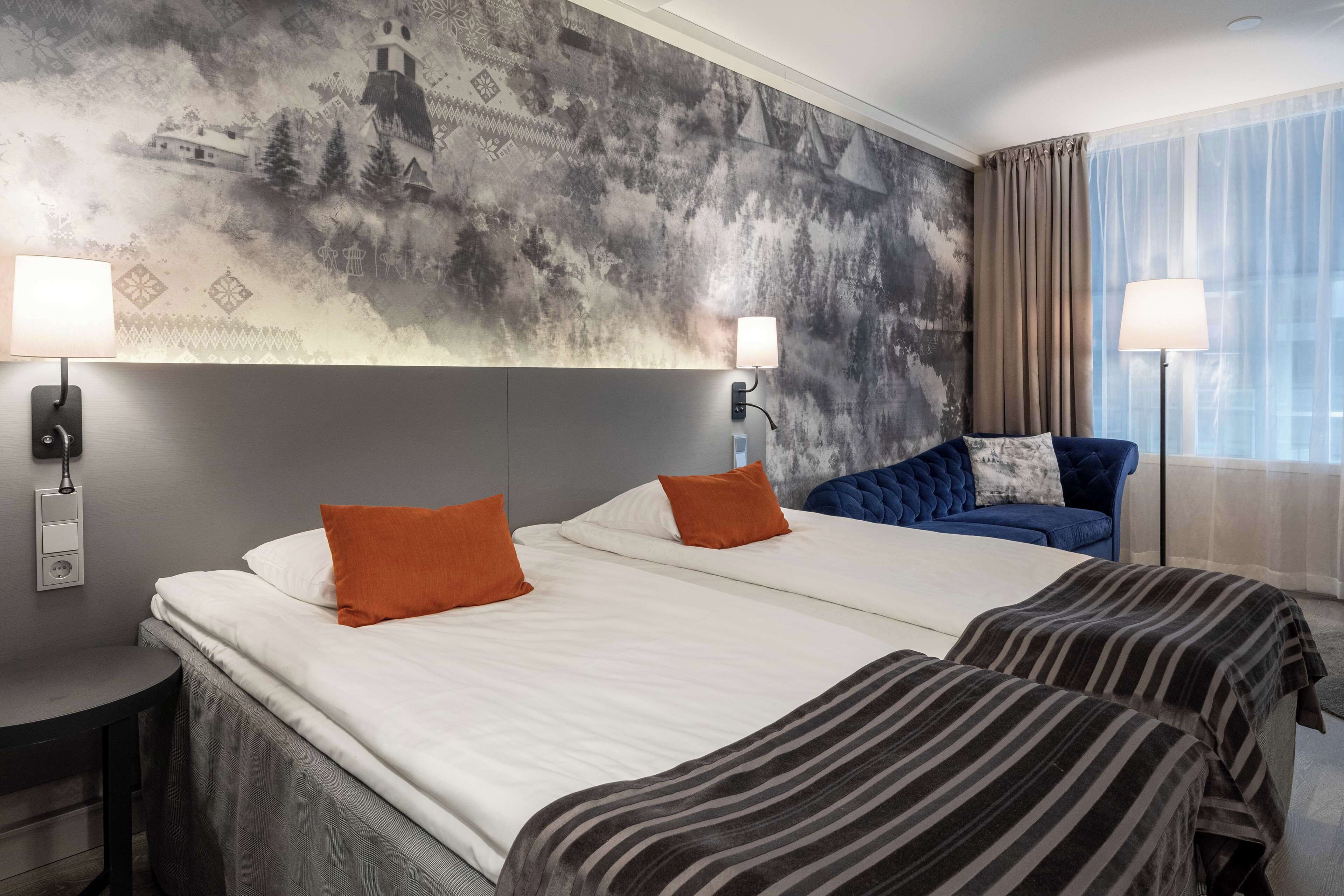 Habitación de hotel con dos camas, un mural grande en la pared y vistas al exterior.