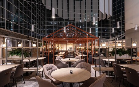 A modern indoor dining area with round tables and chairs, a central wooden structure, and large windows.