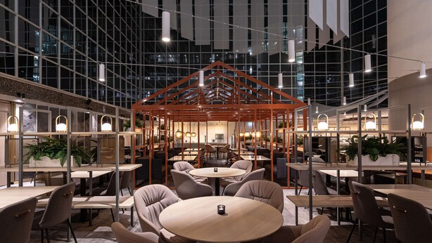 Un espace de restauration intérieur moderne, doté de tables et de chaises rondes, d’une structure centrale en bois et de grandes fenêtres.