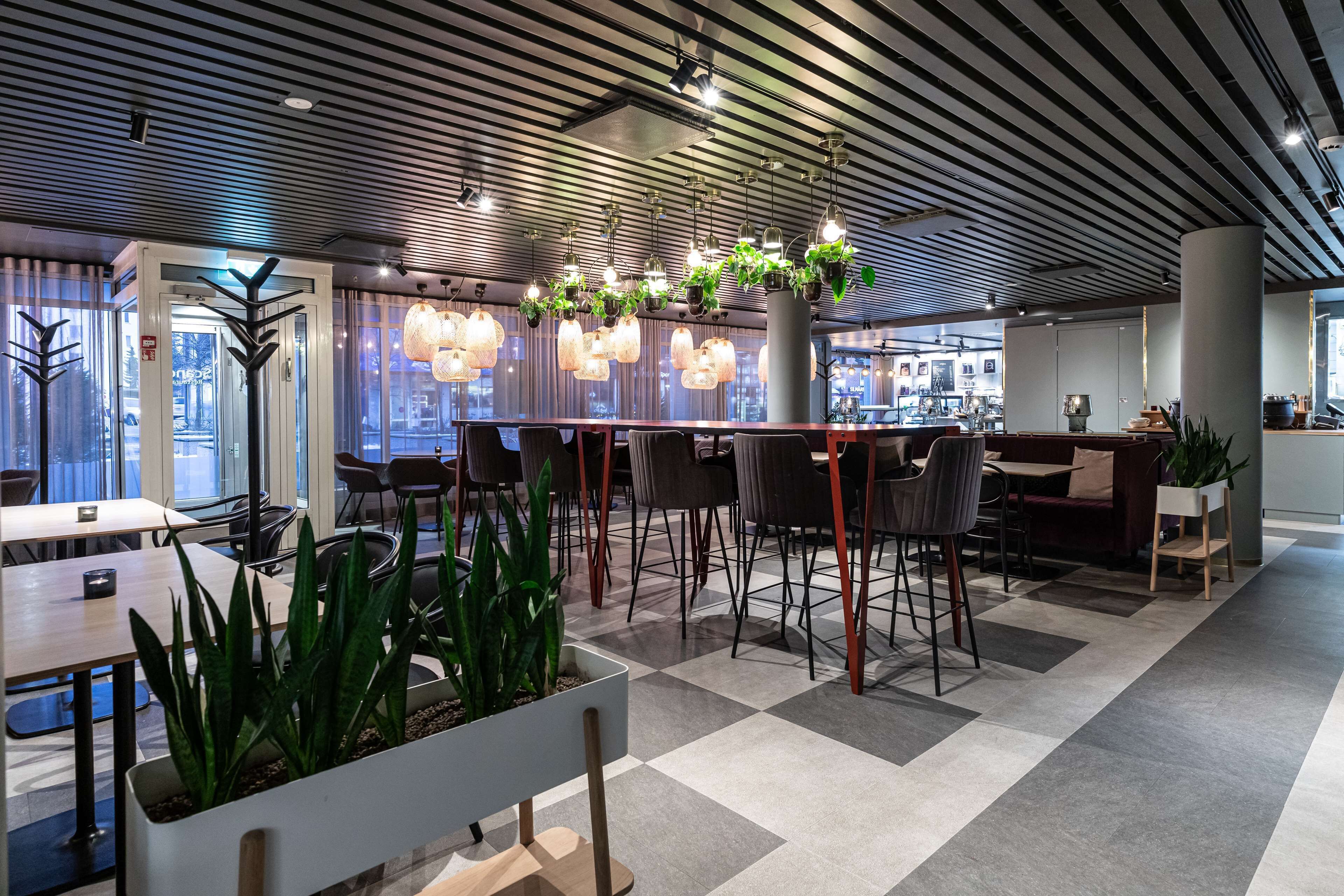 A modern interior with a checkered floor, bar seating, and hanging plants.