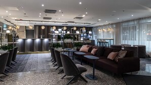 Un hall d’hôtel moderne doté d’un bar, de différents espaces de détente et d’une grande fenêtre laissant entrer la lumière naturelle.