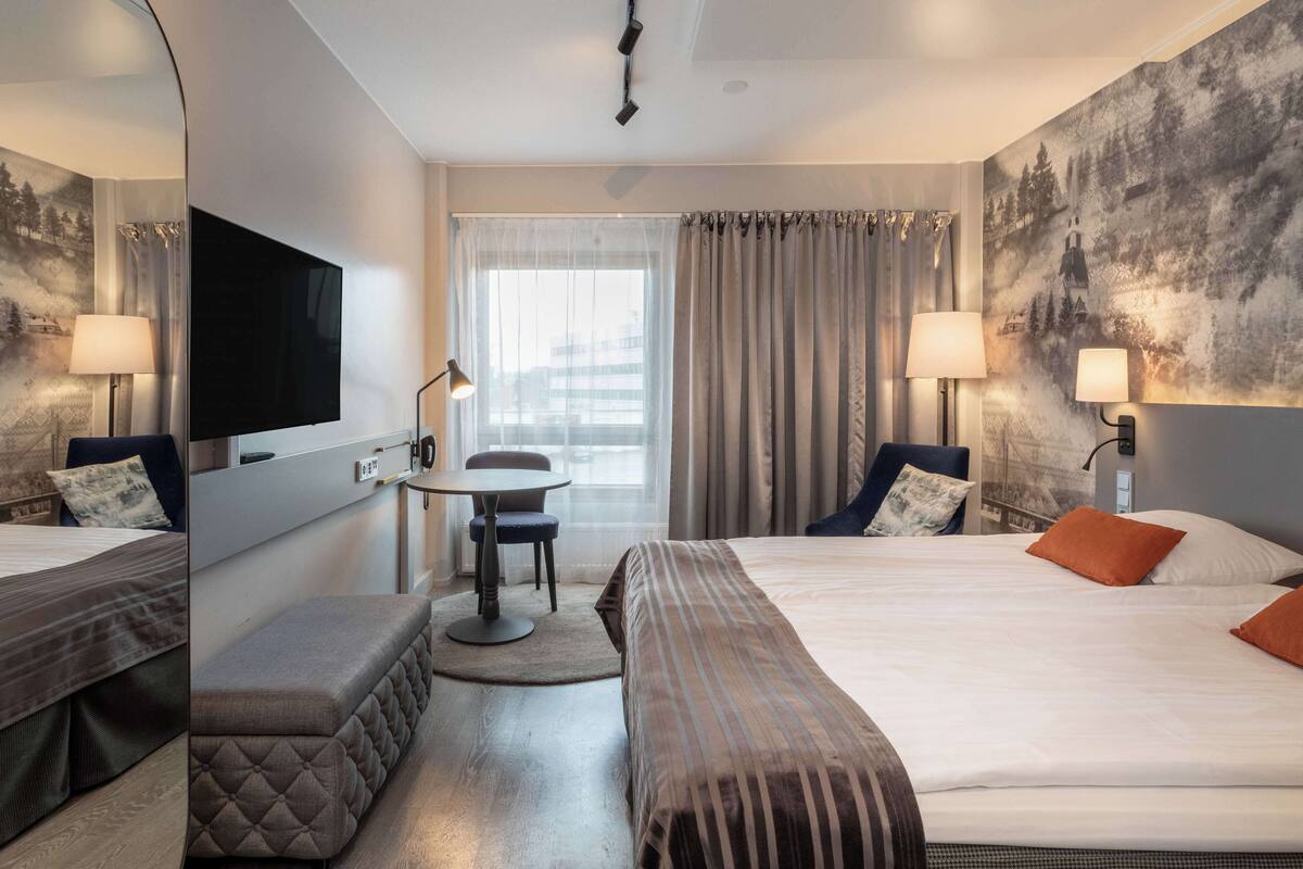A hotel room with a bed, a desk, a chair, a TV, and a large window with curtains.