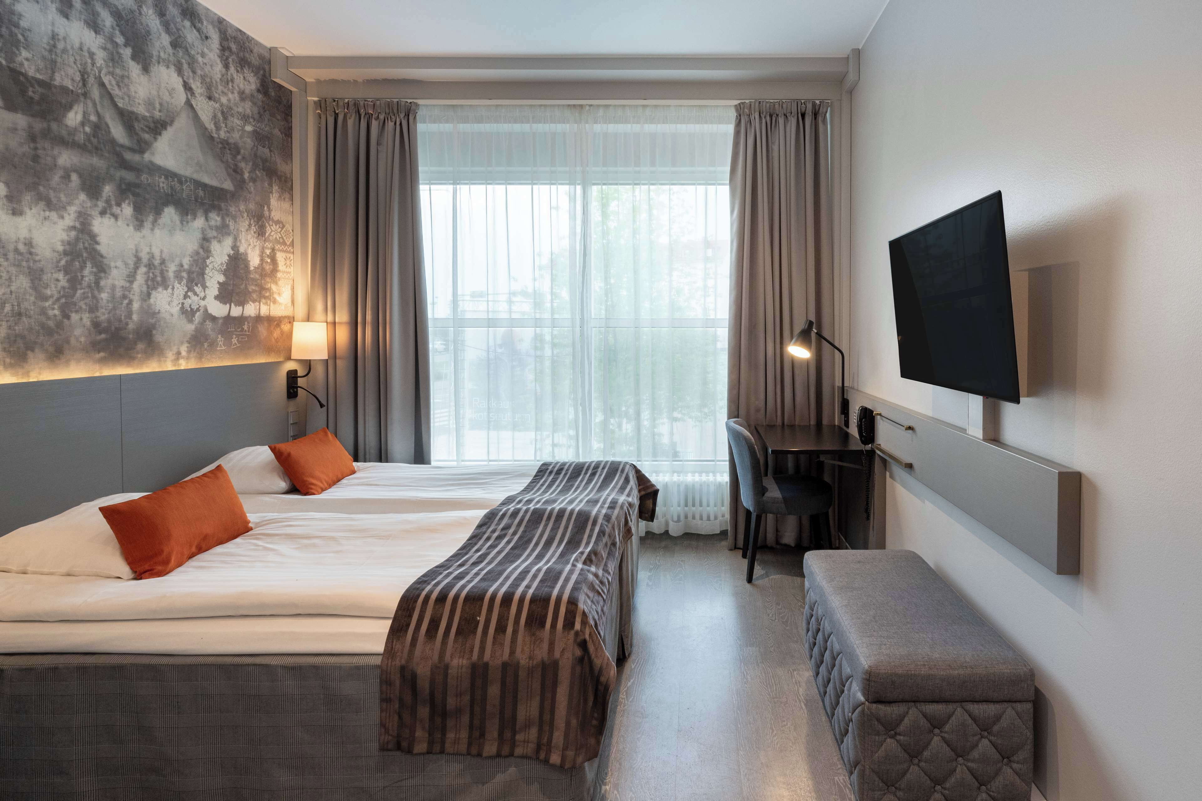 Een hotelkamer met twee bedden, een bureau, een televisie en een groot raam met gordijnen.