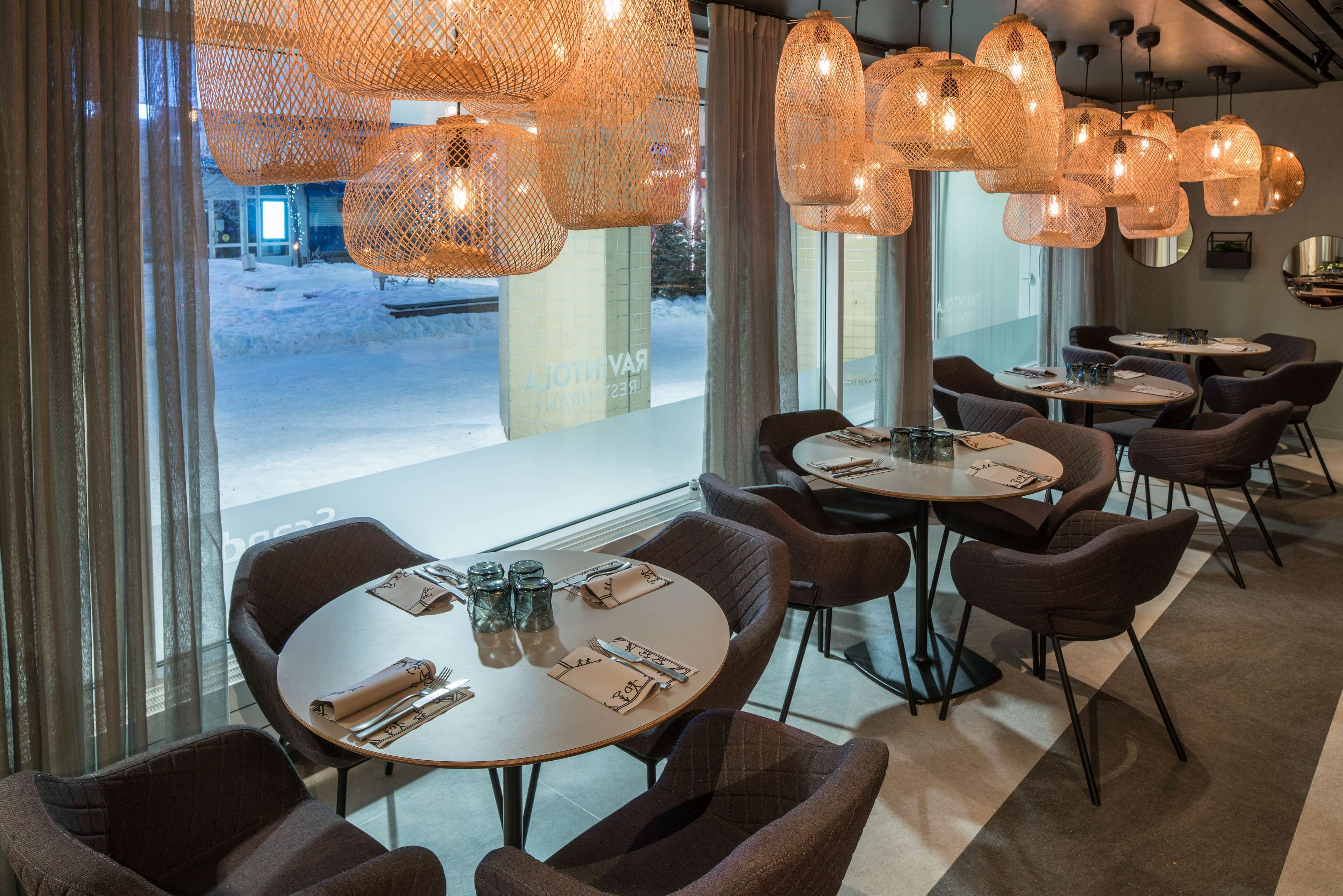 A restaurant interior with round tables, brown upholstered chairs, and woven pendant lights.