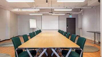 A conference room with a long table, green chairs, a projector screen, and a door.