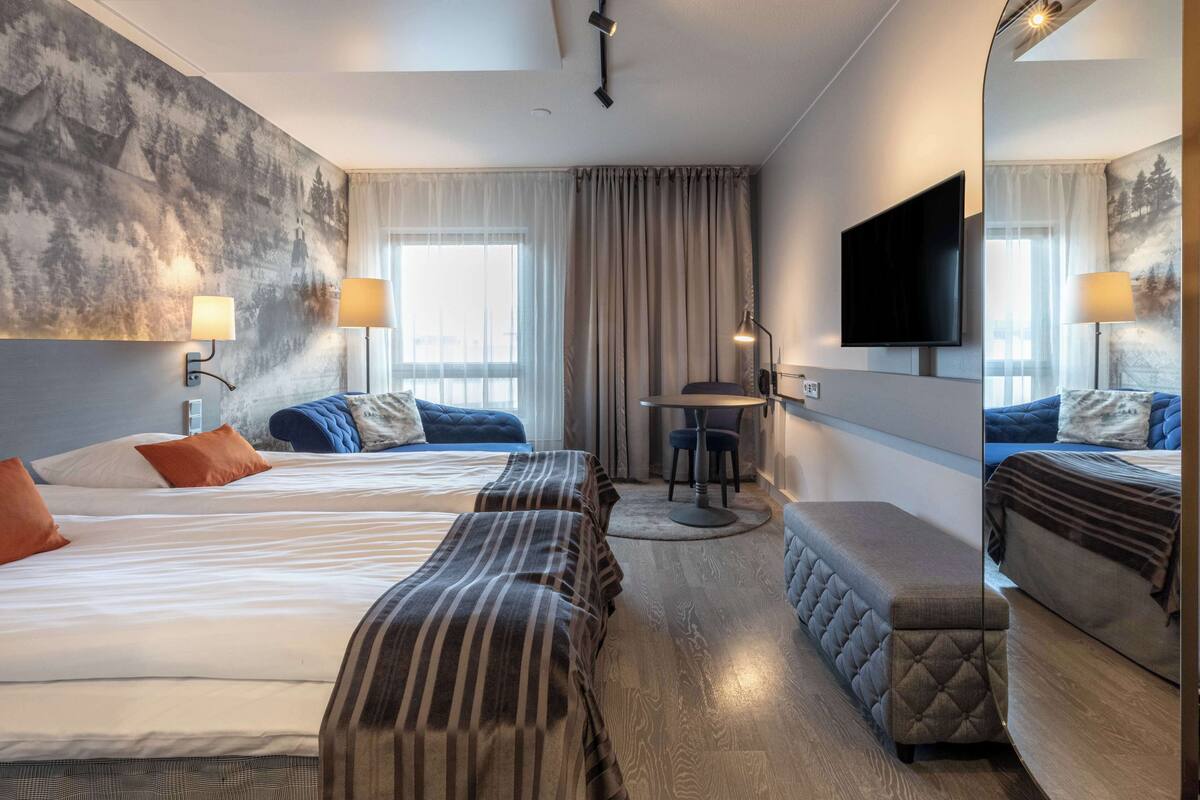 A hotel room with two beds, a desk, a chair, a TV, and a large mirror.
