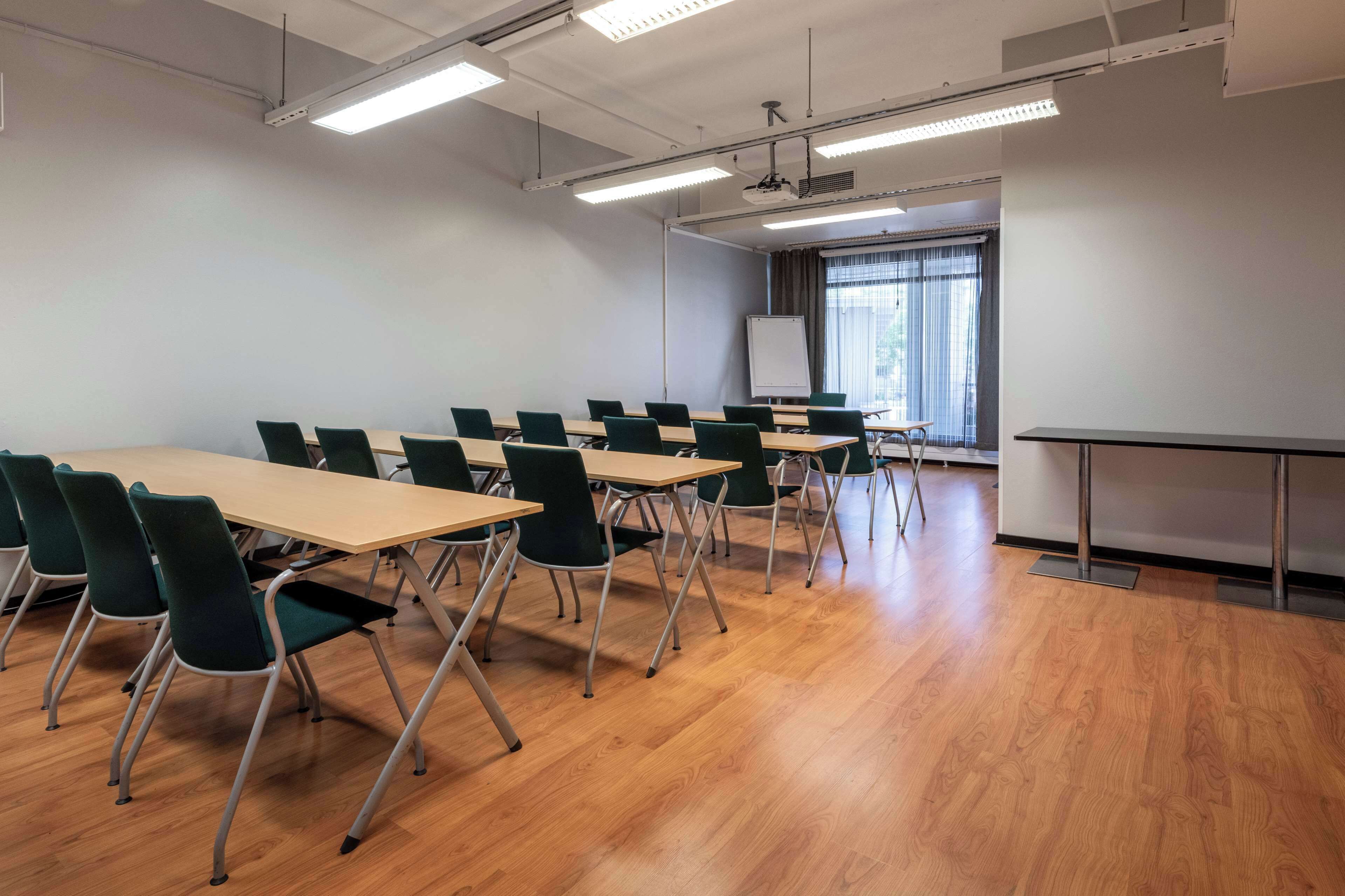 A conference room with a long table, green chairs, a whiteboard, and a projector.