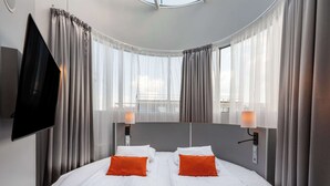 Une chambre d’hôtel avec un lit, deux oreillers, une télévision et des rideaux.