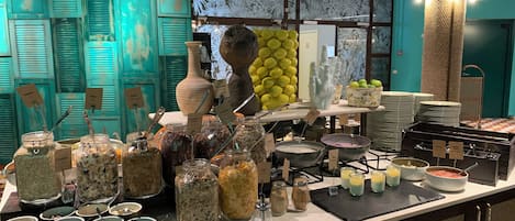 A buffet setup with various food items and containers, including jars of granola and bowls of soup, in a room with teal walls and a patterned ceiling.