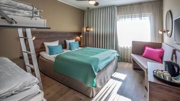 Habitación de hotel con literas, un sofá, un escritorio con una bandeja de objetos y un ventanal con cortinas.