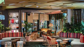 A modern lounge area with a curved sofa, wicker chairs, and a variety of small tables.