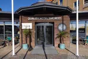 La entrada del Quality Hotel The Reef presenta un diseño moderno, con dos palmeras en macetas y un acceso cubierto.