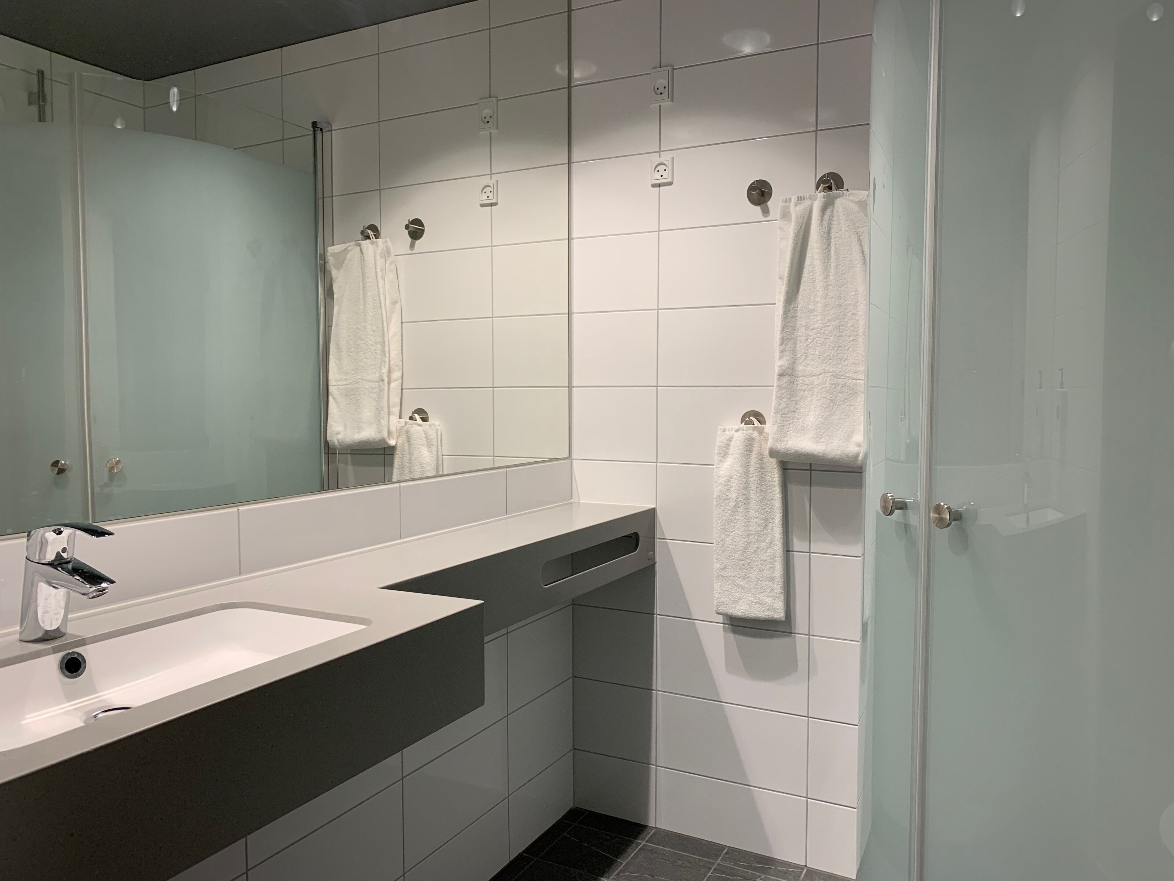A modern bathroom with a large mirror, a sink, and a shower area.